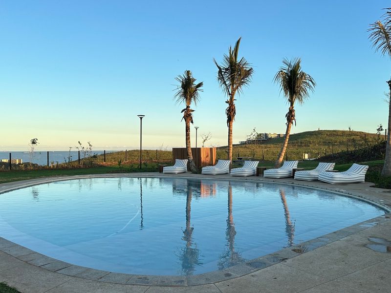 A well-maintained circular swimming pool set within a landscaped area, featuring a paved deck, perimeter fencing, and scenic coastal views.