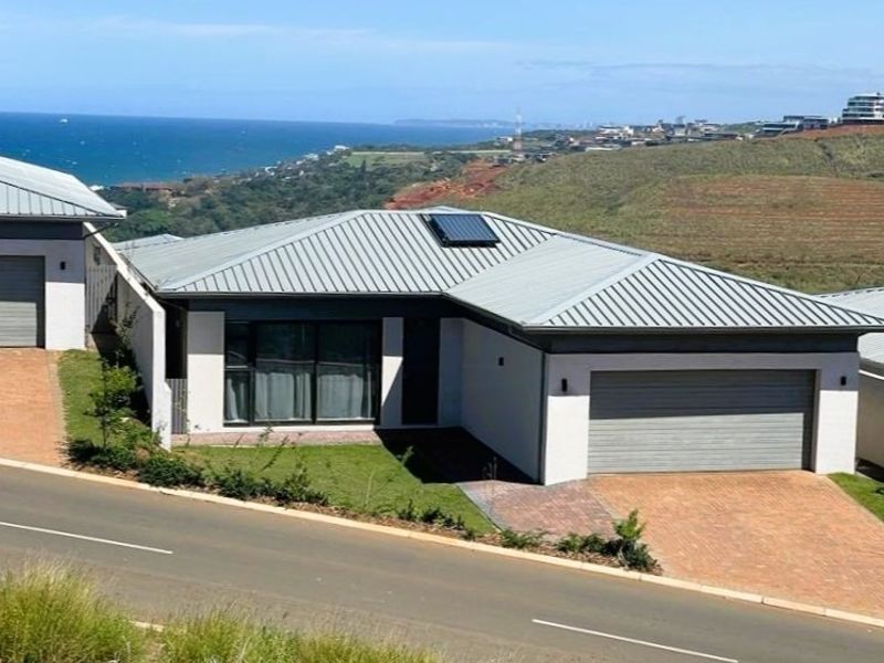 Modern residential property featuring a metal roof, solar water heater, paved driveway, and double garage with scenic coastal views.