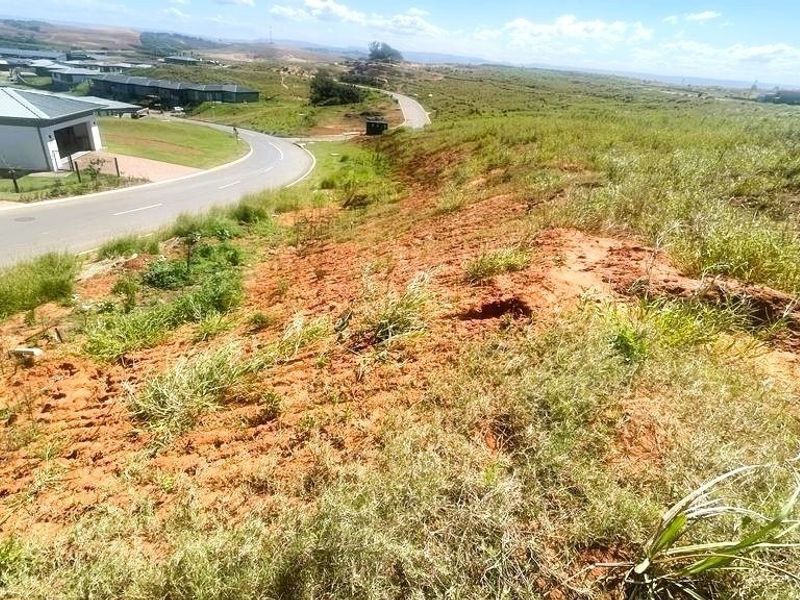An elevated view of a vacant residential plot featuring sloped terrain and direct access to a paved estate road.