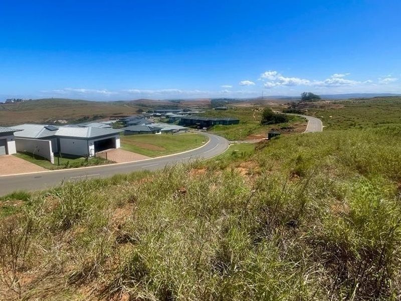 An elevated view of a vacant residential plot overlooking a developed estate with paved roads and modern housing in the distance.