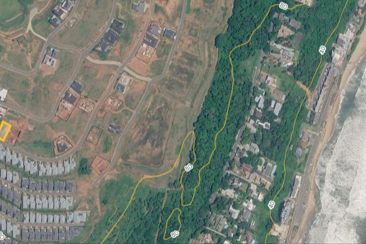 An aerial view of a vacant residential plot located within a coastal estate, highlighting its position relative to the surrounding neighborhood and coastline.