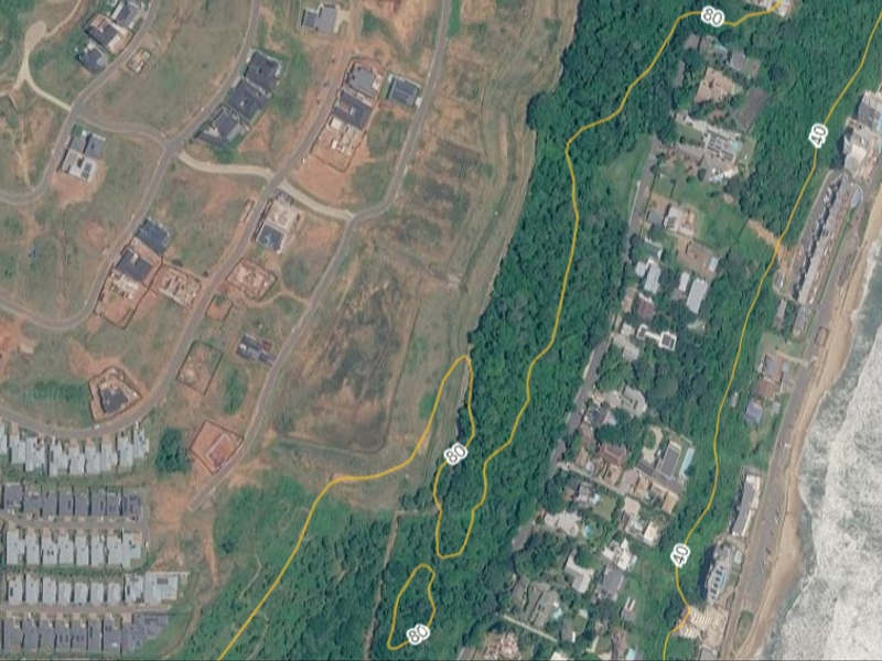 An aerial view of a vacant residential plot located within a coastal estate, highlighting its position relative to the surrounding neighborhood and coastline.