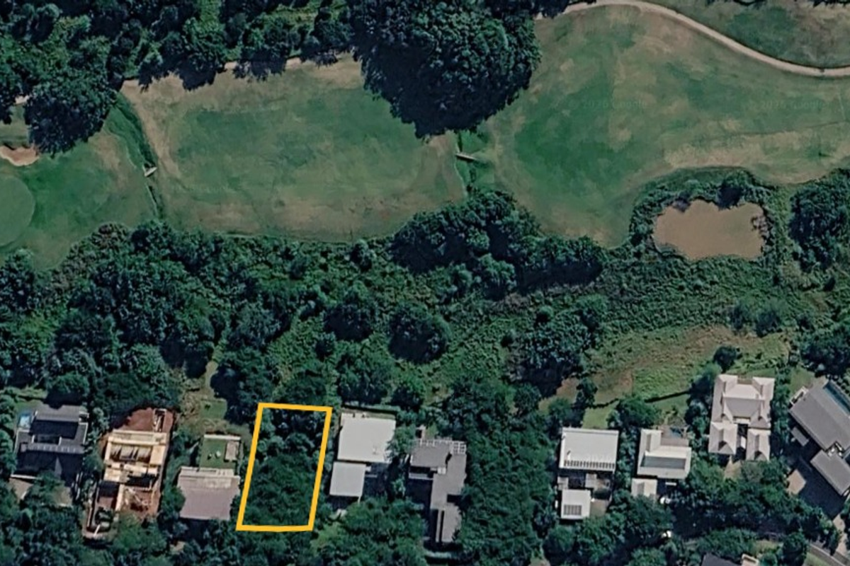 Aerial view of a vacant residential plot situated within a lush, green estate setting, highlighting the property boundaries and surrounding landscape.