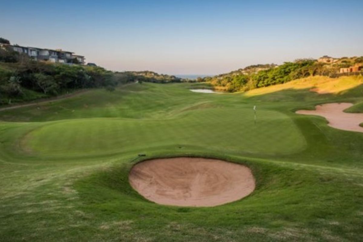 A scenic view of a well-maintained golf course featuring rolling greens, sand bunkers, and distant coastal landscape.