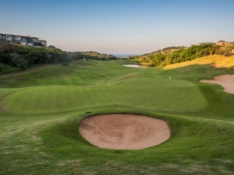 A scenic view of a well-maintained golf course featuring rolling greens, sand bunkers, and distant coastal landscape.
