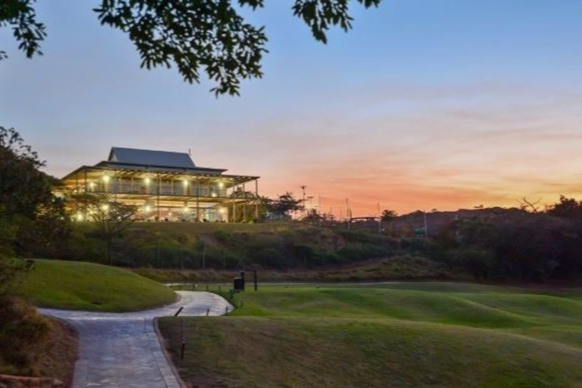 A scenic view of a multi-level residential property set against a sunset, featuring a paved pathway leading towards the elevated dwelling.