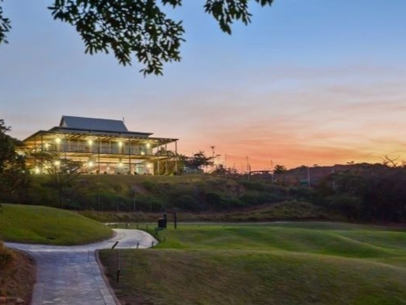 A scenic view of a multi-level residential property set against a sunset, featuring a paved pathway leading towards the elevated dwelling.