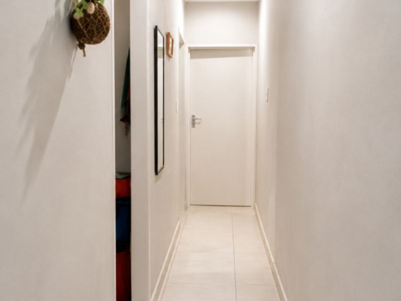 A clean, well-lit hallway featuring neutral tiled flooring, recessed ceiling lighting, and crisp white walls, providing a bright transition between living spaces.