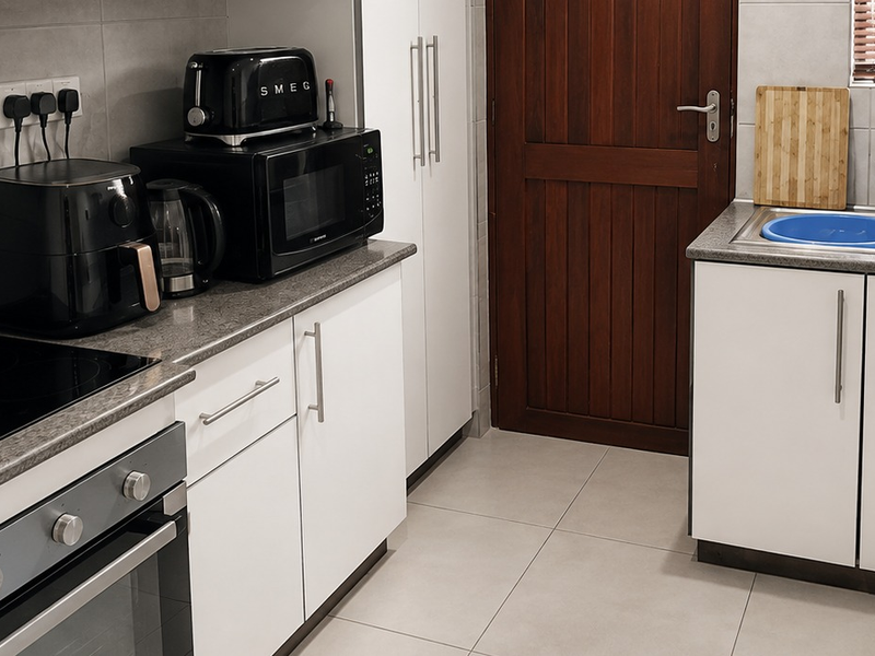 A functional kitchen featuring white cabinetry, stone-look countertops, a built-in oven with electric hob, and a stainless steel sink with tiled splashback.