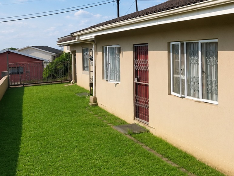 A rear exterior view of the property featuring a lawn area, security gates, and windows with security bars.