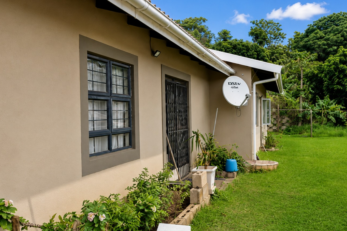 Rear exterior view of the property featuring a well-maintained lawn, security gate, and satellite dish installation.