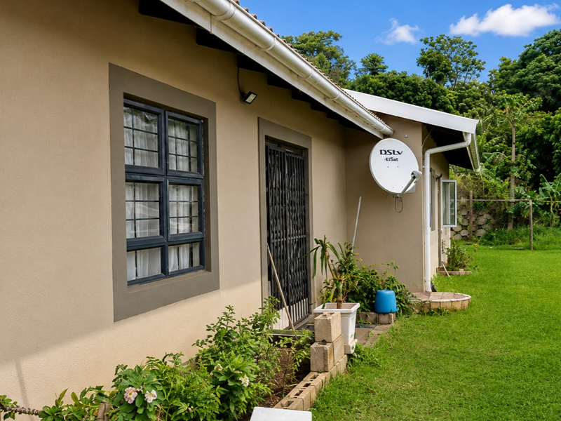 Rear exterior view of the property featuring a well-maintained lawn, security gate, and satellite dish installation.