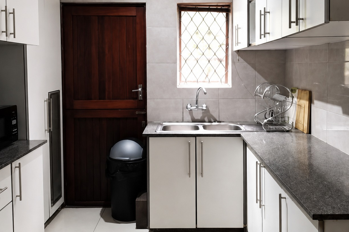 A functional kitchen featuring white cabinetry, dark laminate countertops, a double bowl stainless steel sink, and tiled finishes.