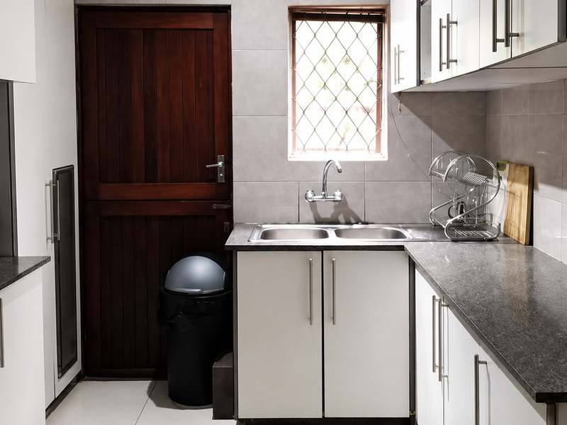 A functional kitchen featuring white cabinetry, dark laminate countertops, a double bowl stainless steel sink, and tiled finishes.