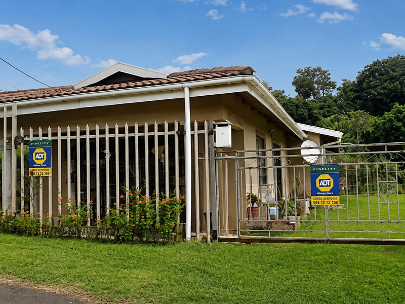 Front exterior view of a single-story house featuring a tiled roof, security gate, and perimeter fencing set within a grassed yard.