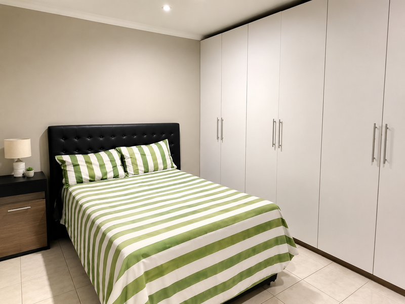 A well-maintained bedroom featuring neutral walls, tiled flooring, recessed downlighting, and extensive floor-to-ceiling built-in cupboards for ample storage.
