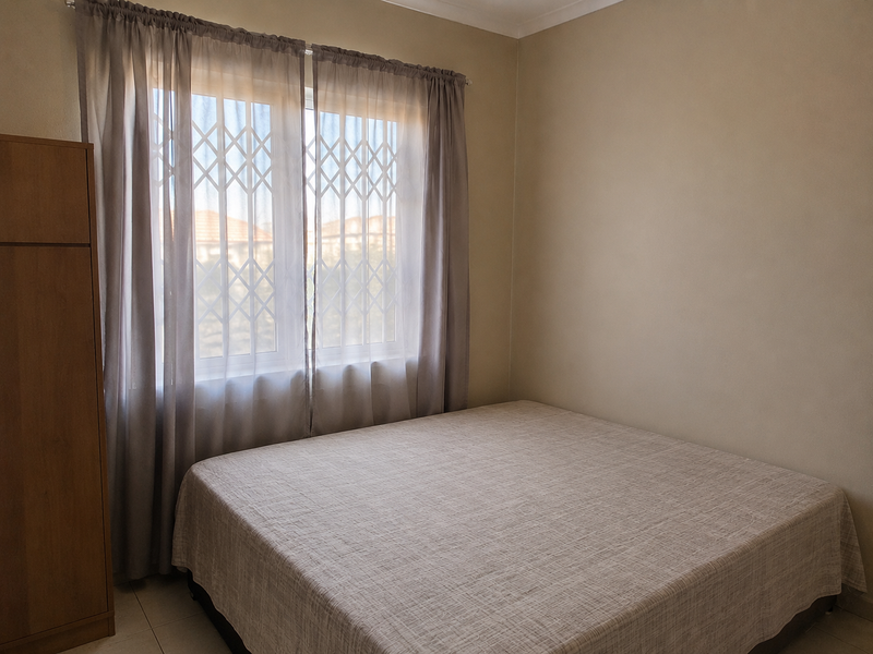 A simple bedroom featuring tiled flooring, a built-in wardrobe, and a window fitted with a security gate.