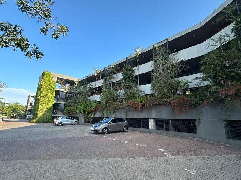 Exterior view of a multi-story apartment building featuring a paved parking area, concrete facade, and integrated vertical landscaping.