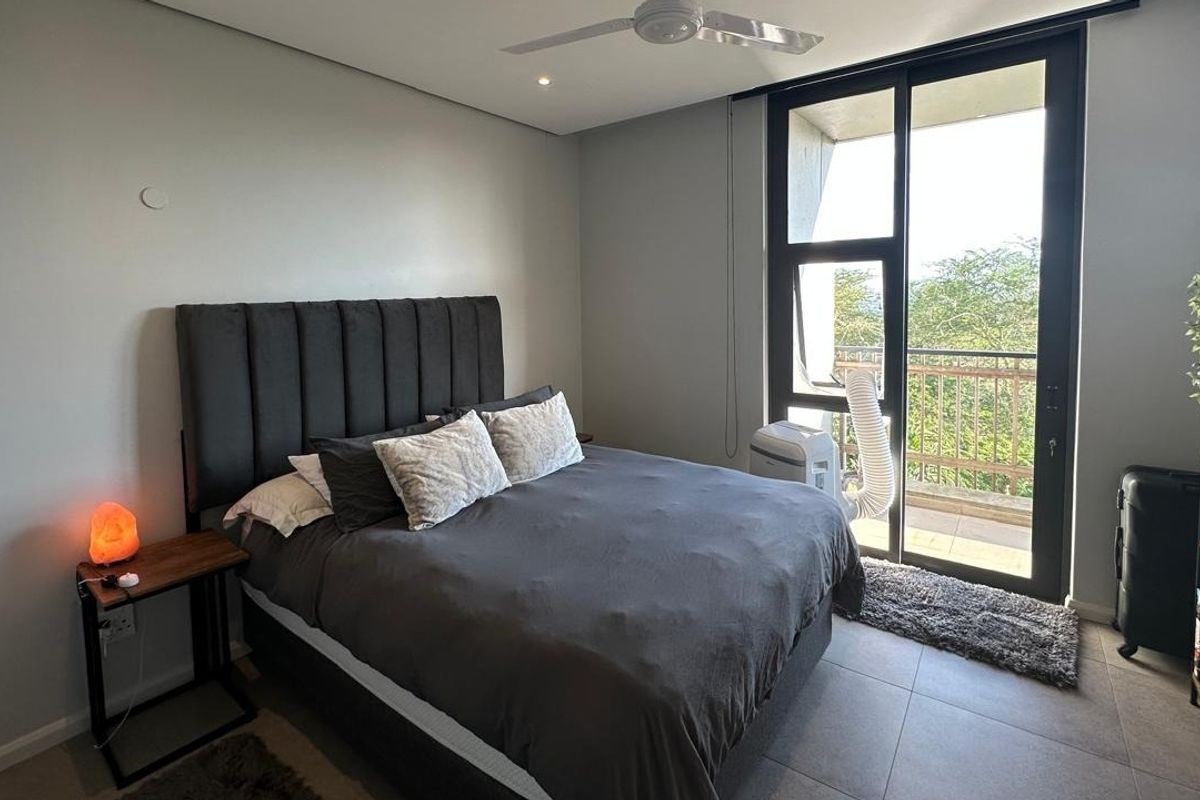 A well-maintained bedroom featuring tiled flooring, a ceiling fan, and a large sliding glass door providing access to a private balcony.