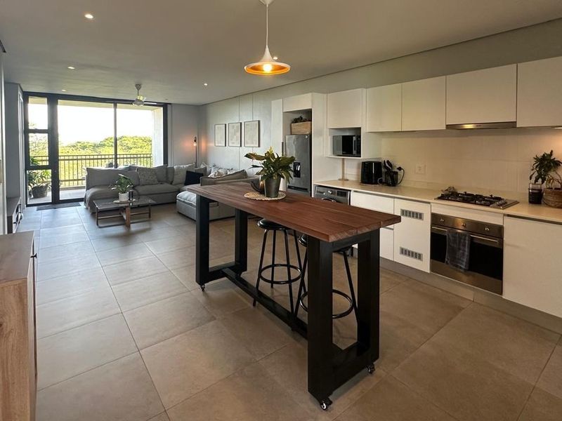 Modern open-plan living area featuring a sleek kitchen with built-in appliances, tiled floors, and seamless access to a balcony with scenic views.