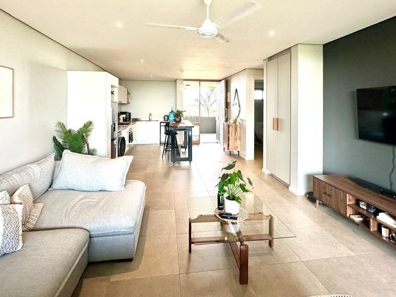 Modern open-plan living area featuring tiled floors, recessed lighting, a ceiling fan, and a seamless transition to the kitchen and outdoor balcony.
