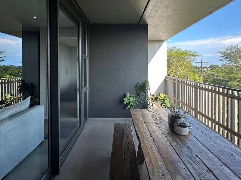 A modern covered balcony featuring tiled flooring, a timber slat balustrade, and large sliding glass doors providing seamless indoor-outdoor flow.
