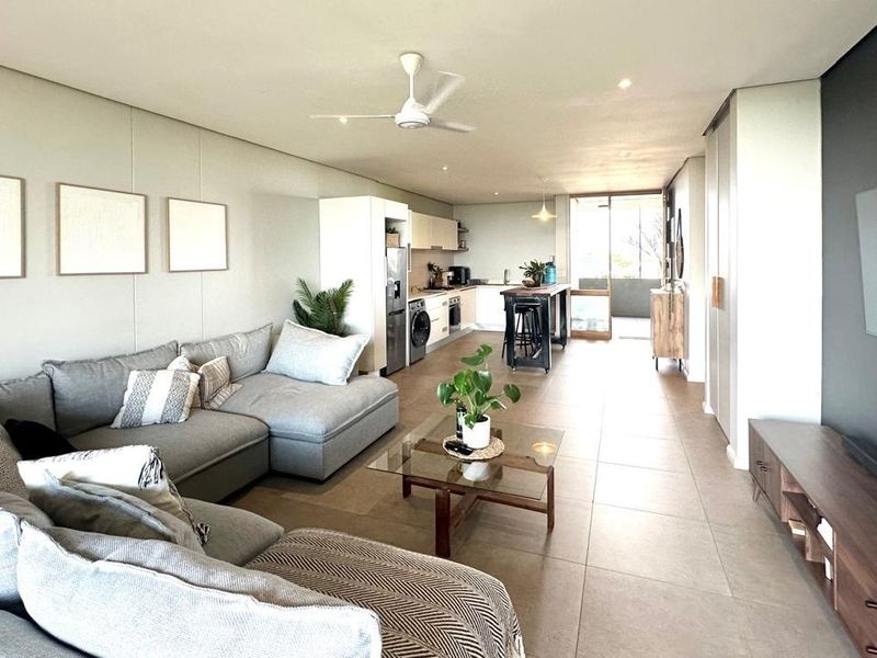 Spacious open-plan living area featuring tiled floors, recessed lighting, a ceiling fan, and a modern kitchen with integrated cabinetry leading to a balcony.