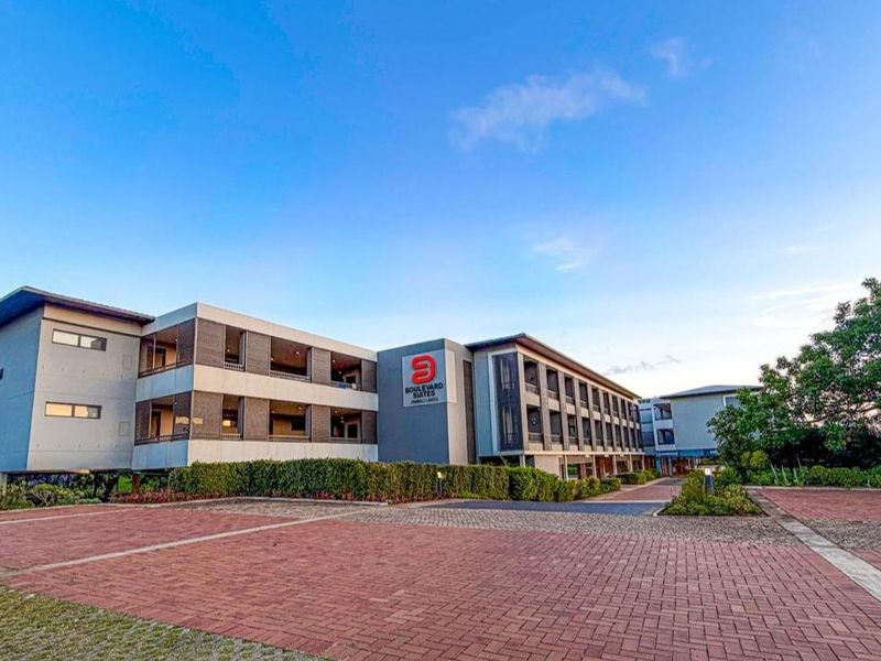 Exterior view of the Boulevard Suites apartment complex featuring a paved driveway, landscaped gardens, and multi-story building facade with balconies.