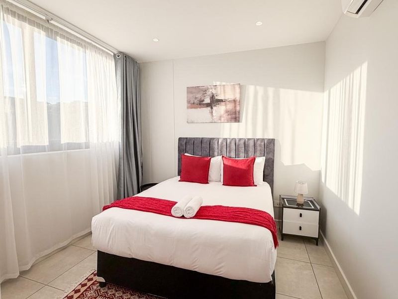 A bright and modern bedroom featuring tiled flooring, recessed lighting, and a wall-mounted air conditioning unit, offering a clean and comfortable living space.