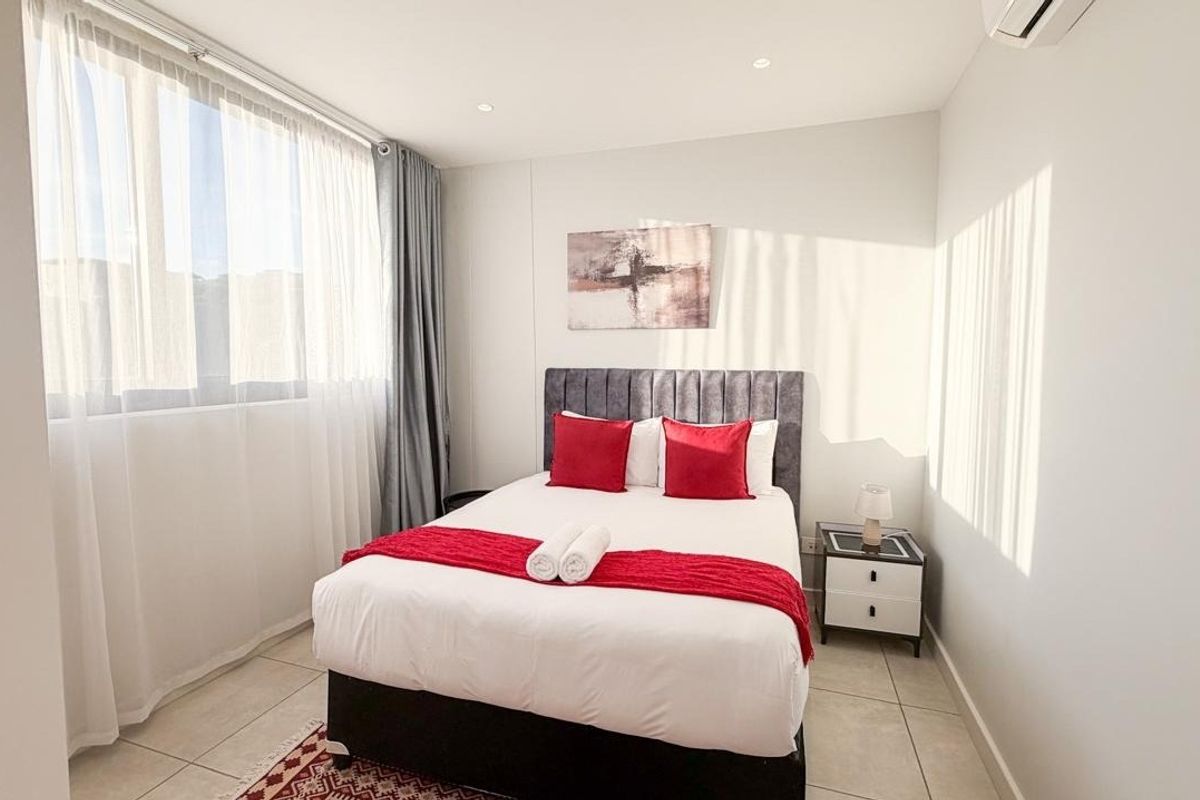 A bright and modern bedroom featuring tiled flooring, recessed lighting, and a wall-mounted air conditioning unit, offering a clean and comfortable living space.