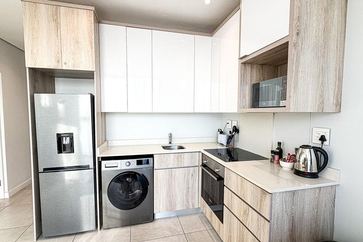 Modern kitchen featuring light wood-grain cabinetry, white high-gloss upper cabinets, stone countertops, and integrated stainless steel appliances.