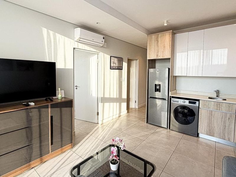 Modern open-plan living area featuring a sleek kitchen with built-in cabinetry, tiled flooring, and an integrated air conditioning unit.