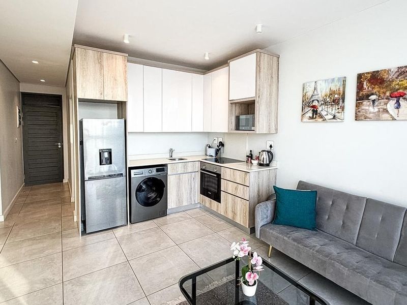 Modern open-plan apartment featuring a compact kitchen with built-in cabinetry, integrated appliances, and neutral tiled flooring throughout the living area.
