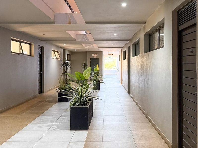 A well-maintained apartment building hallway featuring tiled flooring, recessed lighting, and multiple unit entrance doors.