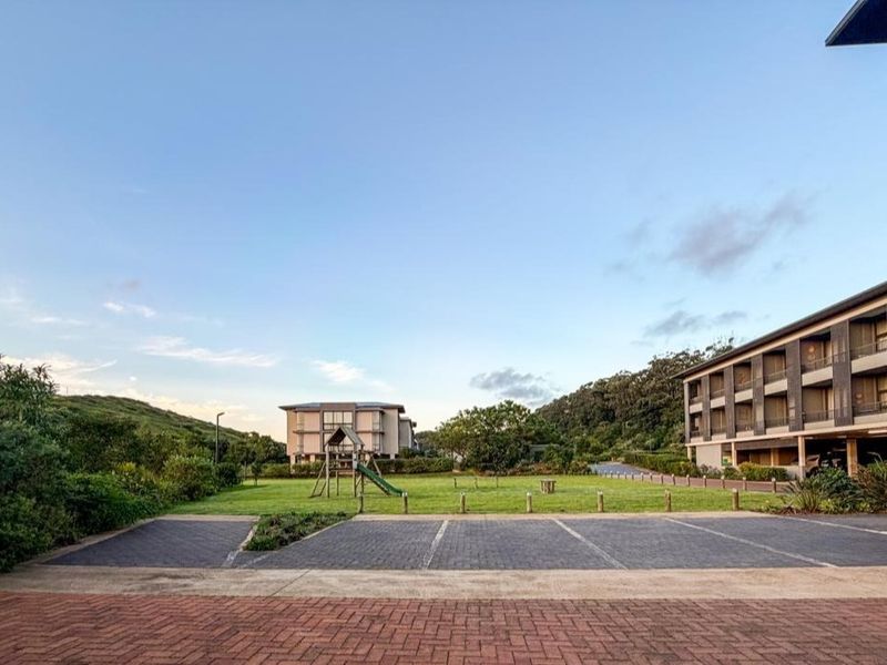 A view of the apartment complex exterior featuring a paved parking area, landscaped lawn, and communal outdoor space.