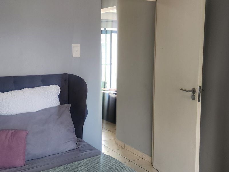 A bedroom interior featuring grey painted walls, tiled flooring, and a doorway leading to an adjacent living space.