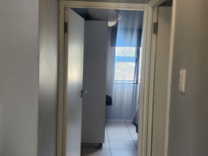 A view through a hallway leading into a bedroom, featuring tiled flooring and neutral wall finishes.