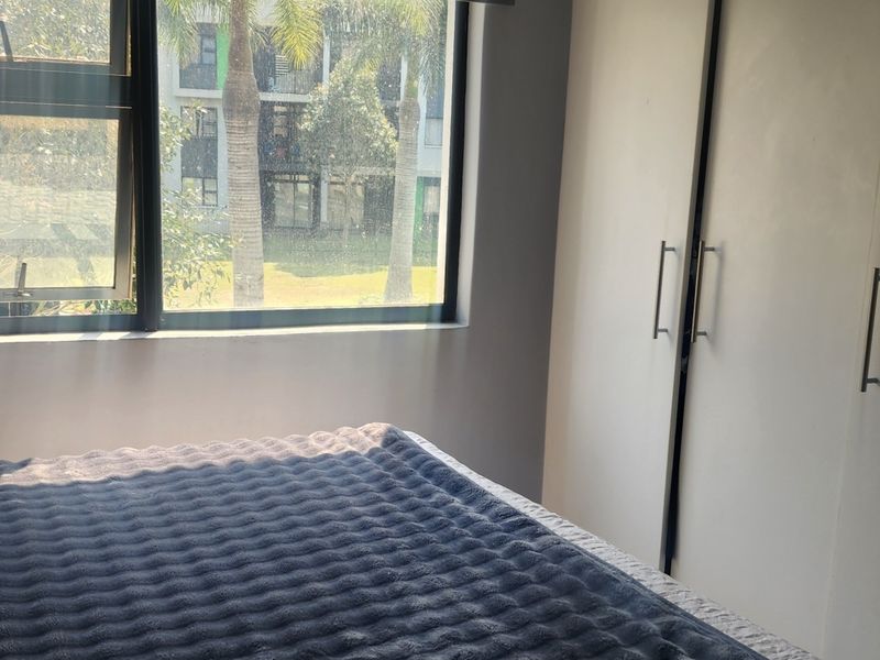 A bedroom featuring built-in cupboards and a large window with views of the surrounding complex.