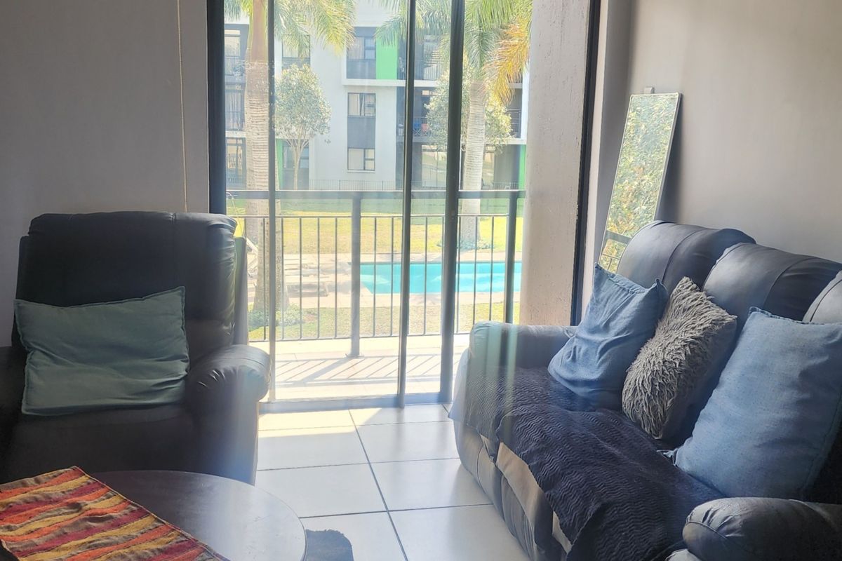 Living room area featuring large sliding glass doors that open onto a balcony with views of the complex pool and garden.