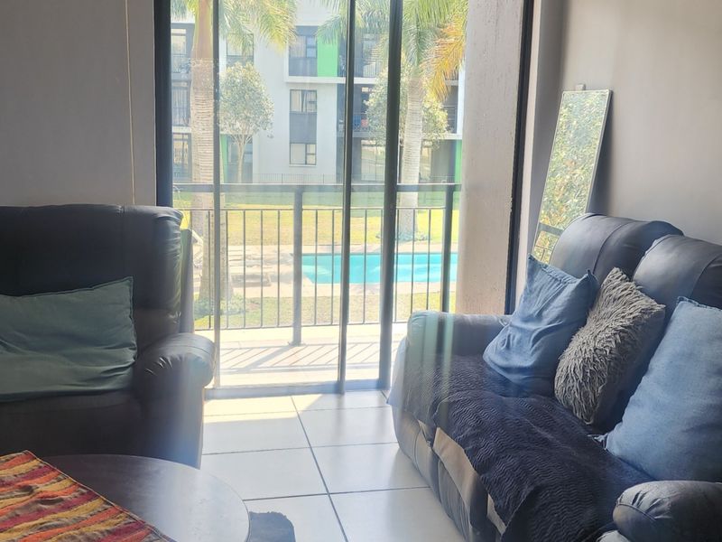 Living room area featuring large sliding glass doors that open onto a balcony with views of the complex pool and garden.