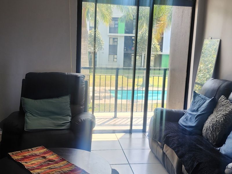 A living room featuring tiled flooring and a large sliding glass door that provides access to a balcony with views of the complex pool.
