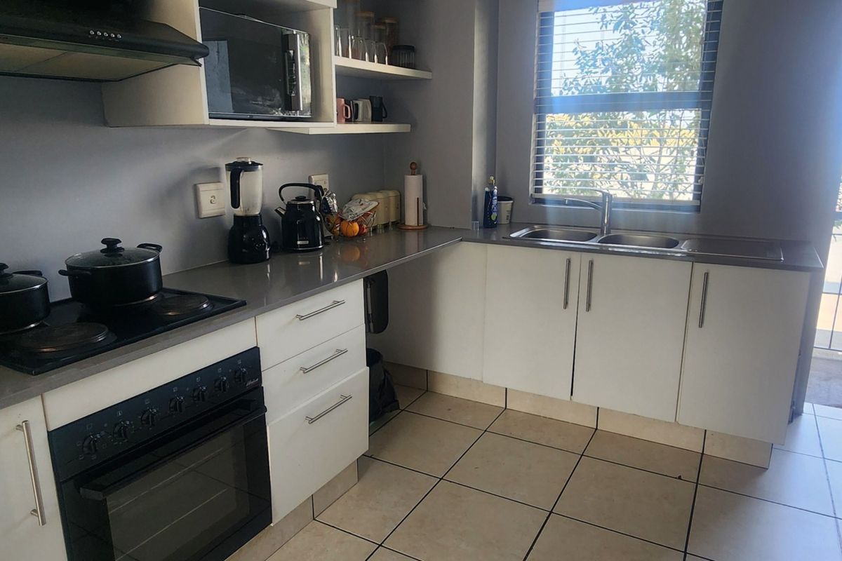 Modern kitchen featuring stone countertops, built-in oven with hob, extractor fan, and ample cabinetry, with natural light from an adjacent balcony window.