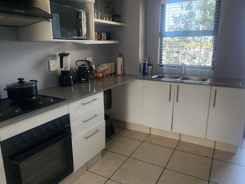 Modern kitchen featuring stone countertops, built-in oven with hob, extractor fan, and ample cabinetry, with natural light from an adjacent balcony window.