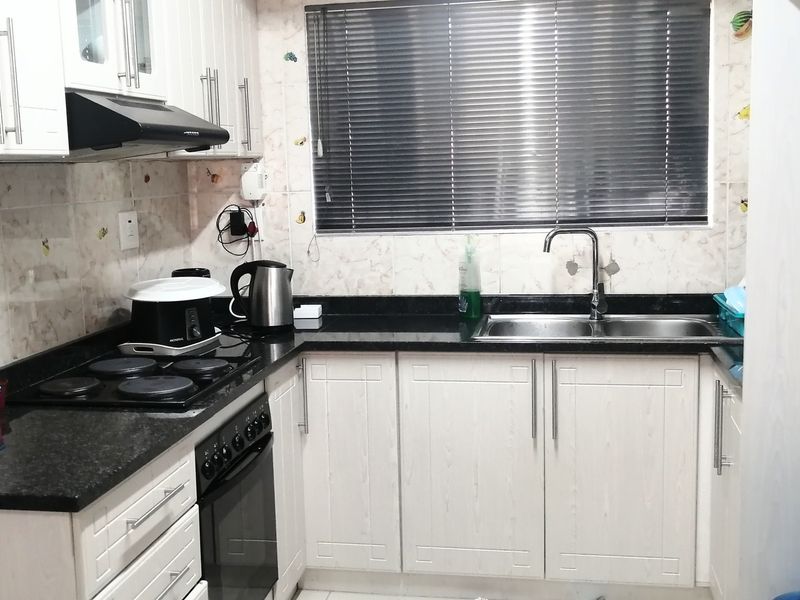A functional kitchen featuring white cabinetry, dark granite countertops, a double basin sink, and integrated electric cooking appliances.