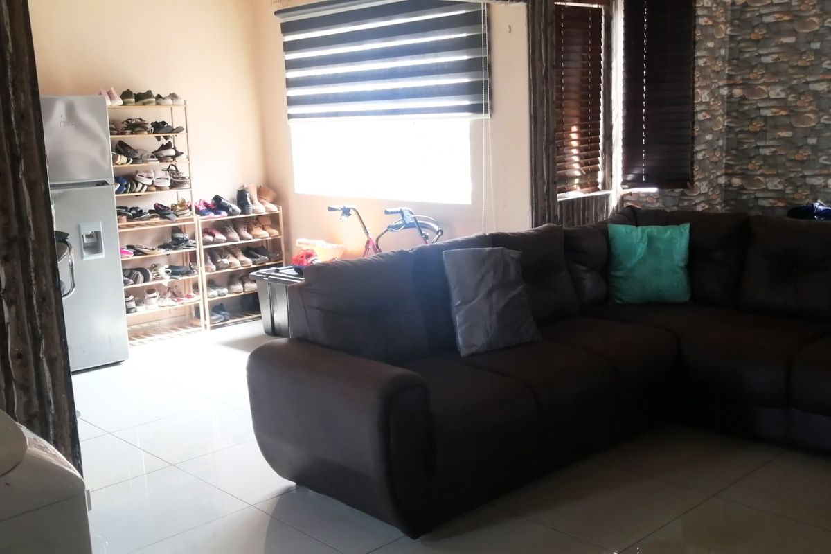 A living room featuring tiled flooring, venetian blinds, and a stone-cladding feature wall, offering a functional space for relaxation.
