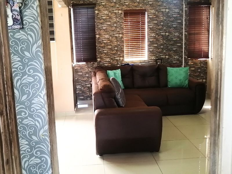 A living room featuring tiled flooring, venetian blinds, and a stone-effect feature wall, viewed from an adjacent doorway.