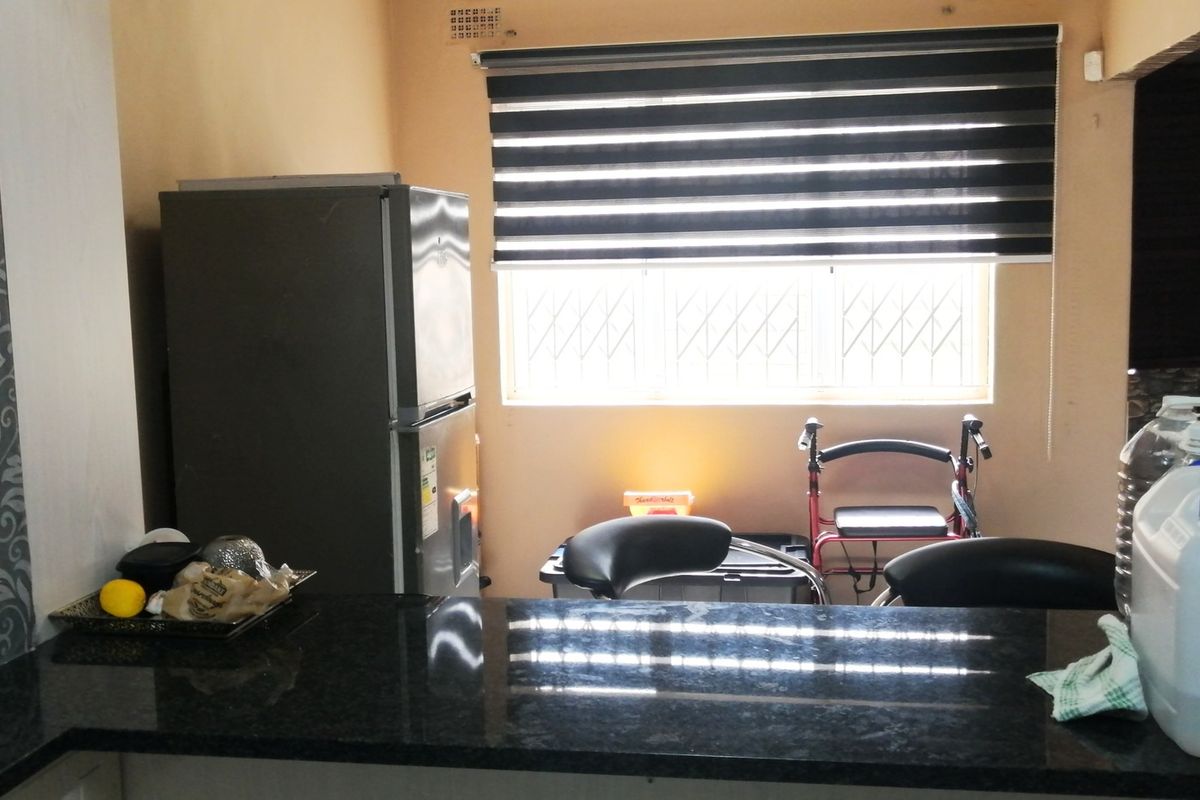 A functional kitchen area featuring dark granite countertops, built-in cabinetry, and a window fitted with security bars and modern roller blinds.