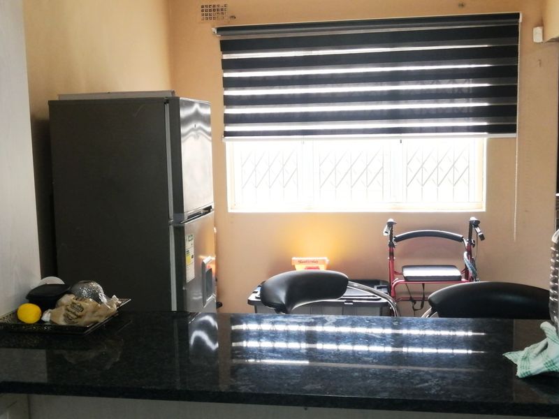 A functional kitchen area featuring dark granite countertops, built-in cabinetry, and a window fitted with security bars and modern roller blinds.