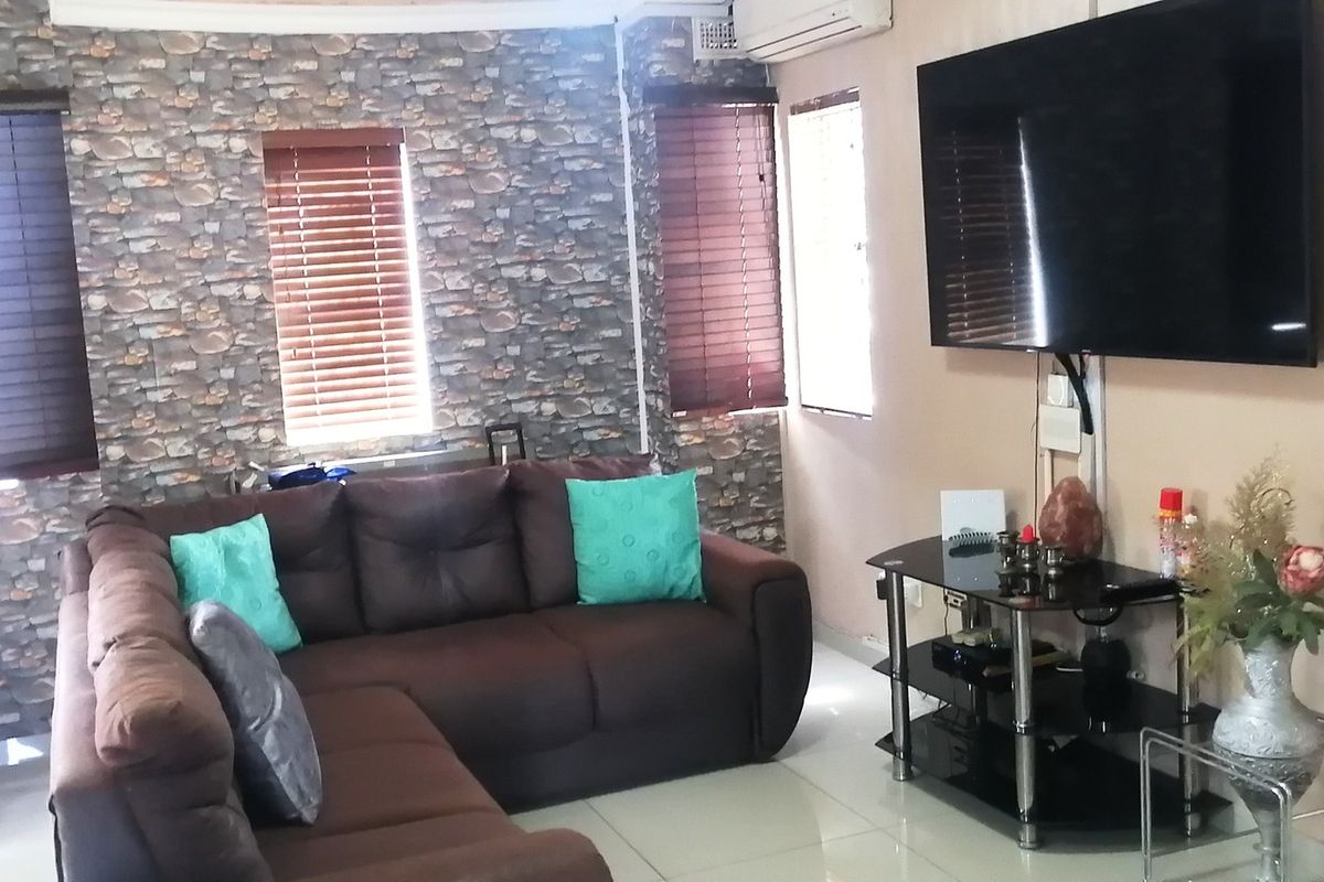 A living room featuring tiled flooring, stone-effect feature wallpaper, venetian blinds, and a wall-mounted air conditioning unit.