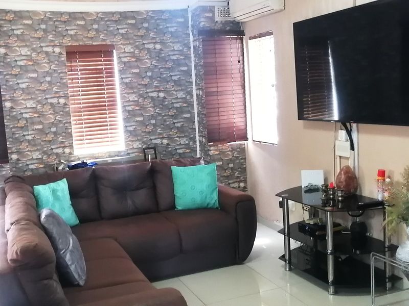 A living room featuring tiled flooring, stone-effect feature wallpaper, venetian blinds, and a wall-mounted air conditioning unit.